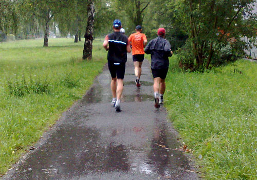 Läufer im Regen auf Parkweg mit Pfützen