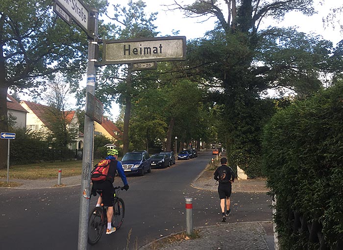 Läufer und Radbegleiter unter Straßenschild „Heimat“