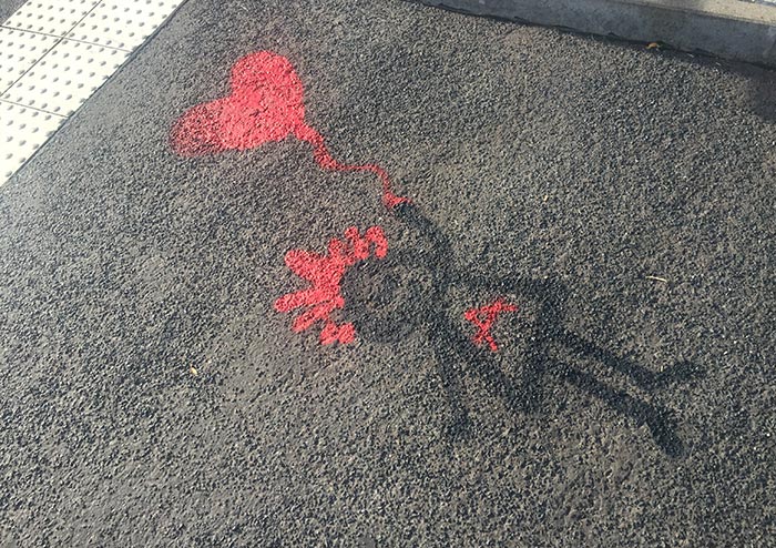 Graffiti auf dem grauen Fußweg: Mädchen mit roten Haaren und rotem Herz-Luftballon