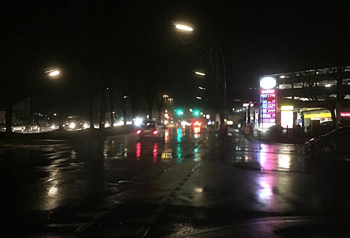 Regennasse Straße mit Lichter-Spiegelungen in der Dunkelheit