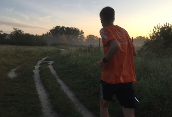 Läufer auf Feldweg bei Sonnenaufgang und Morgennebel
