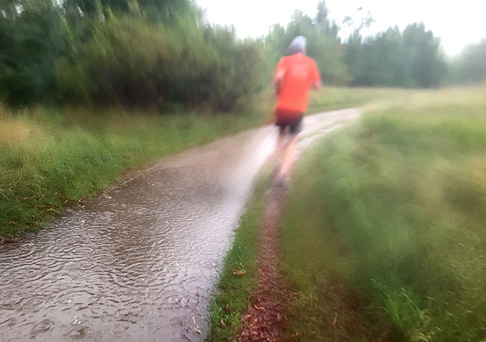 Läufer bei strömendem Regen im Park neben einer großen Pfütze