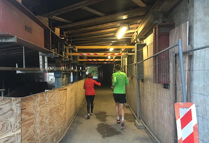 Läuferin und Läufer in Unterführungsbaustelle mit Neonlicht
