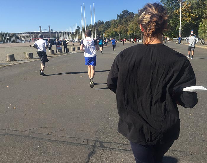Läuferin mit Corona-Maske am Arm läuft auf das Olympiastadion zu