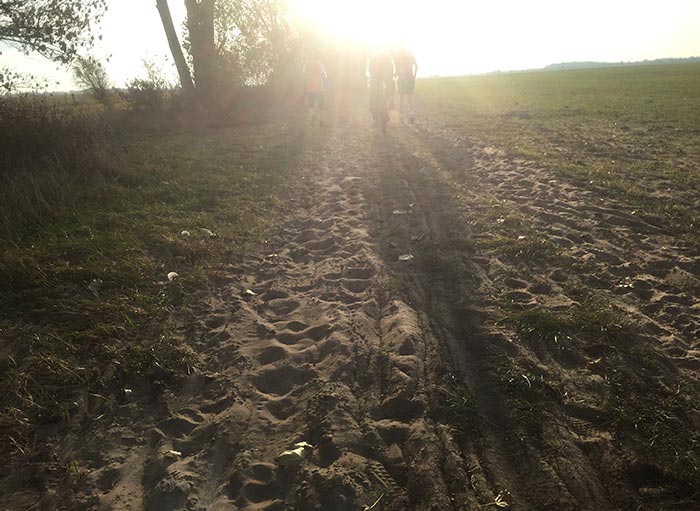 Sandiger Weg, im Sonnen-Gegenlicht zwei Läufer und ein Radfahrer