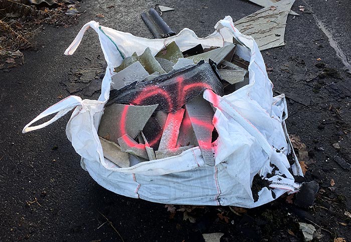 Großer weißer Plastiksack mit Asbest-Resten und mit neonrot aufgesprühtem „OA“
