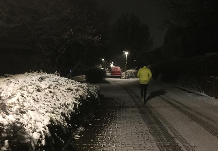 Läufer auf einsamer Straße mit schneebedeckten Büschen