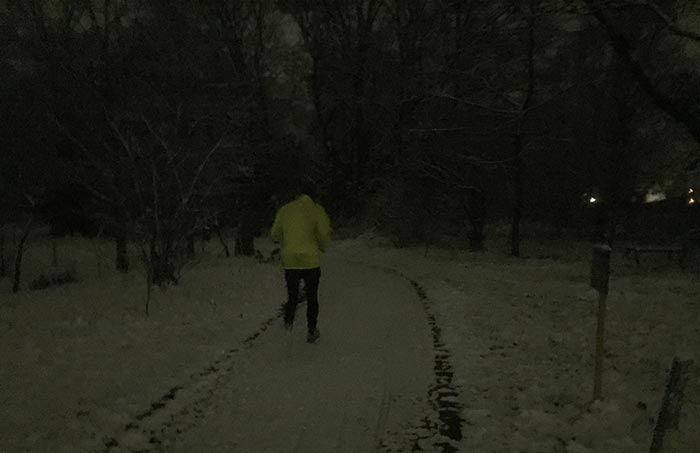Läufer mit neongelber Jacke im schneebedeckten Park