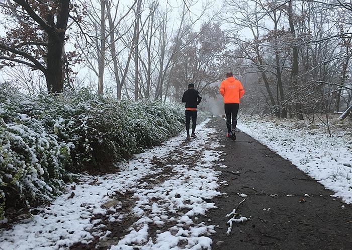 Läufer auf Asphaltweg zwischen Büschen und Bäumen, die zart mit Schnee bedeckt sind