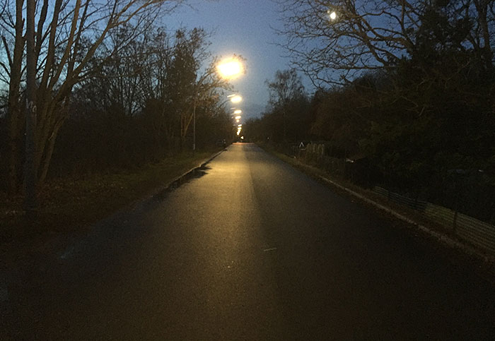 Diedersdorfer Weg, eine einsame Asphalt-Nebenstraße, im Morgendunkel mit Reihe von Laternen