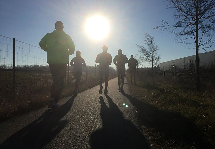 Fünf dunkle Läufer*innen-Silhouetten vor der aufgehenden Morgensonne