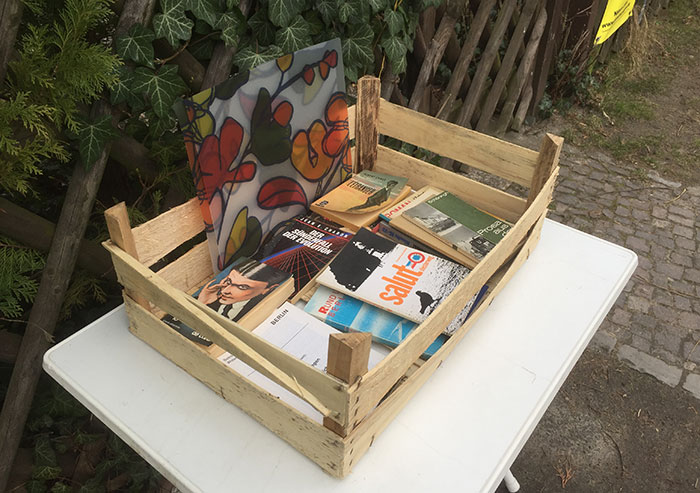 Holzkiste mit gebrauchten Büchern auf einem Plastiktisch vor einem Holzzaun