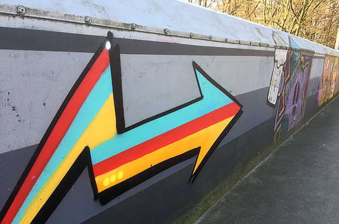 Aufgesprühter blau-rot-gelb gestreifter Graffiti-Pfeil auf der Brücken-Brüstung