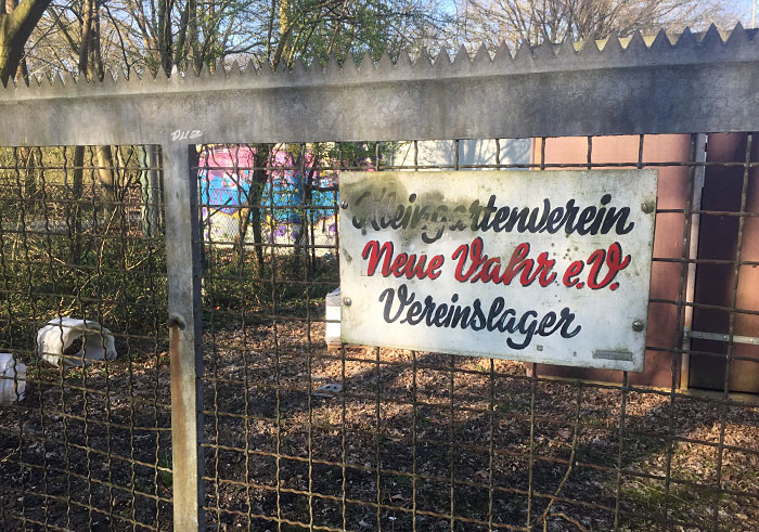 Schild mit alter Typografie an einem Metallzaun: „Kleingartenverein Neue Vahr e.V. Vereinslager“