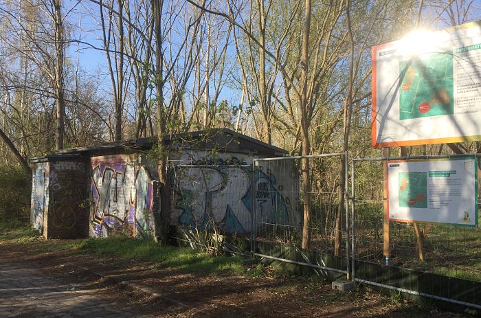 Graffiti-besprühtes Häuschen, daneben Schild und Banner zum geschützten Gebiet
