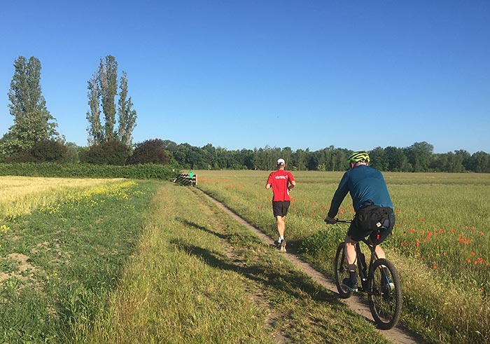 Läufer und Begleit-Radfahrer auf Trampelpfad zwischen Feldern