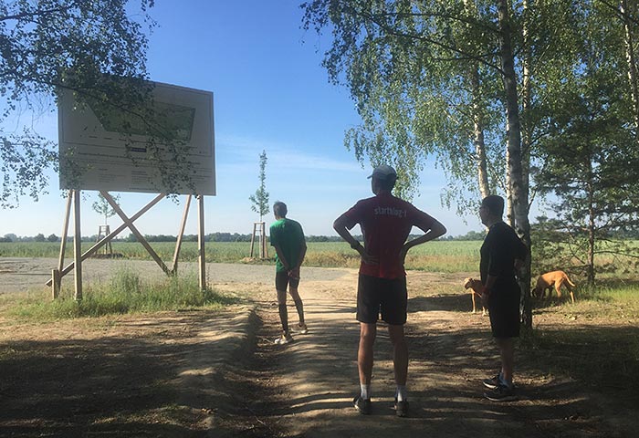 Drei Läufer sehen sich ein großes Schild am Feldrand an