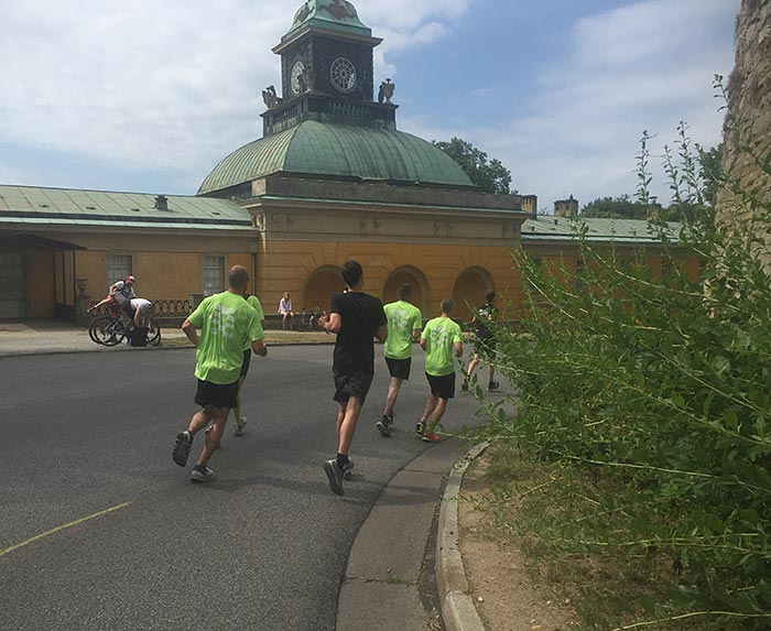 Läufer in den grünen Shirts des Schlösserlaufs in der abfallenden Kurve an einem historischen Gebäude mit gelben Wänden und lindgrünem Kupferdach