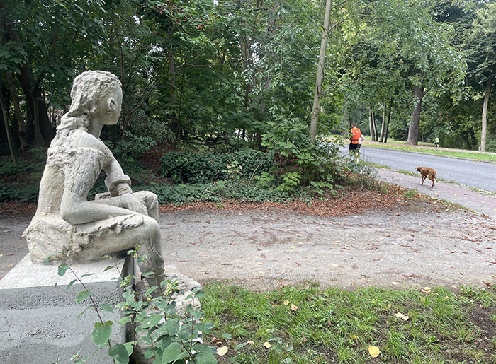 Sitzende Stein-Skulptur scheint Läufern nachzublicken