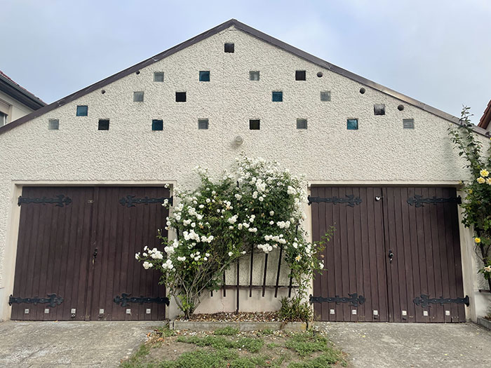 giebelseite eines Gebäudes mit zwei großen symmetrisch angelegten Holztoren, dazwischen ein großer Strauch mit weißen Rosen