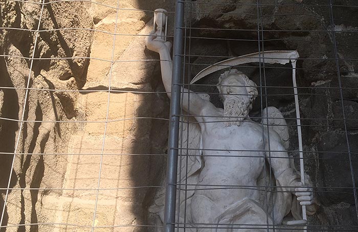 Statue von Chronos mit Sanduhr und Sense hinter einem Bauzaun