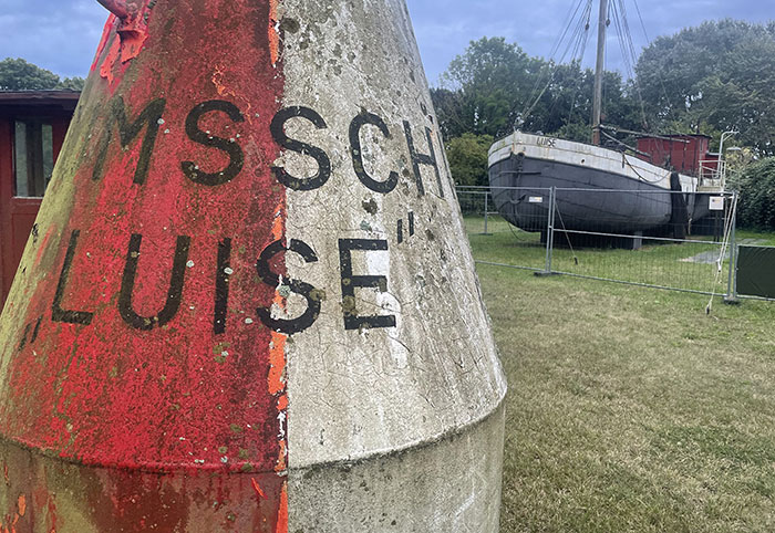 Seeboje mit dem Schriftzug „Luise“ auf dem Rasen, dahinter das Museumsschiff