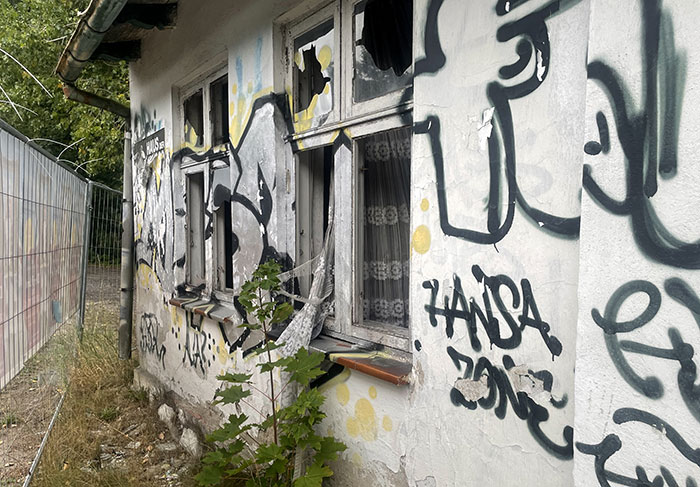 Graffiti-besprühte Fassade mit zerbrochenen Fenstern, durch die alte dreckig-weiße Vorhänge wehen