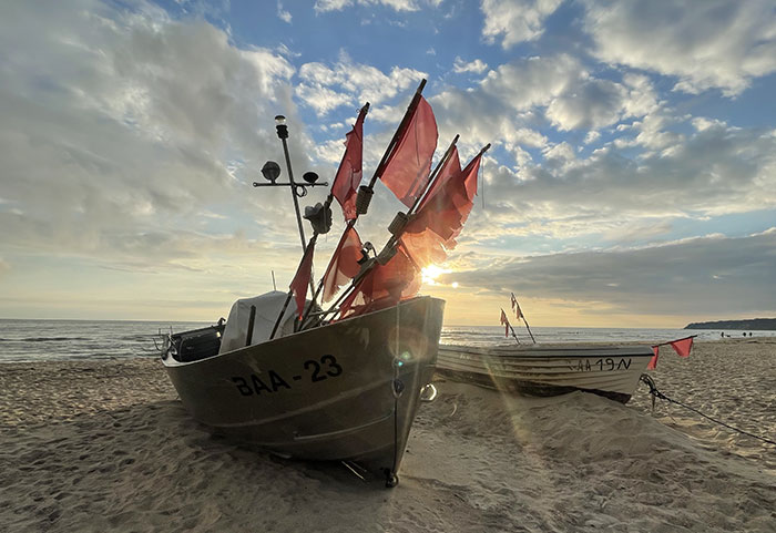 Fischerboot mit roten Fahnen auf dem Sandstrand im Gegenlicht der aufgehenden Sonne