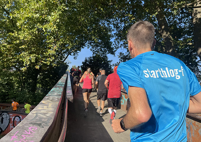 Läufer in hellblauem Shirt mit Aufdruck startblog-f läuft die Steigung der Autobahnbrücke hinauf