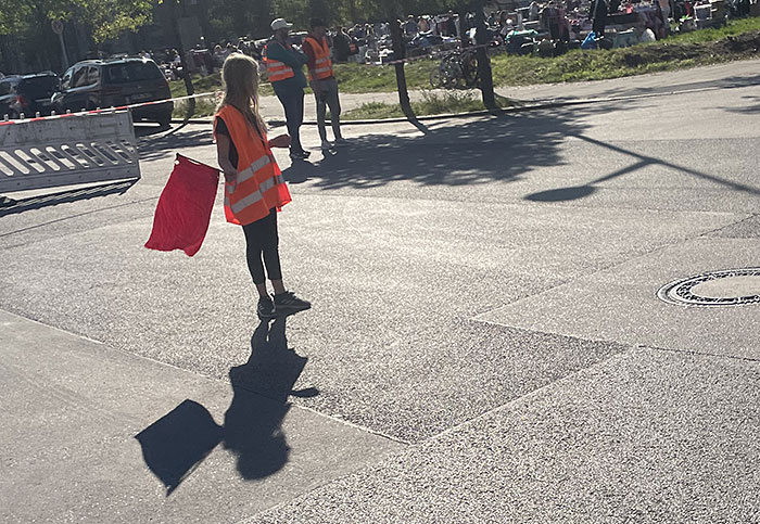 Kleine Helferin in zu großer oranger Warnweste mit roter Fahne
