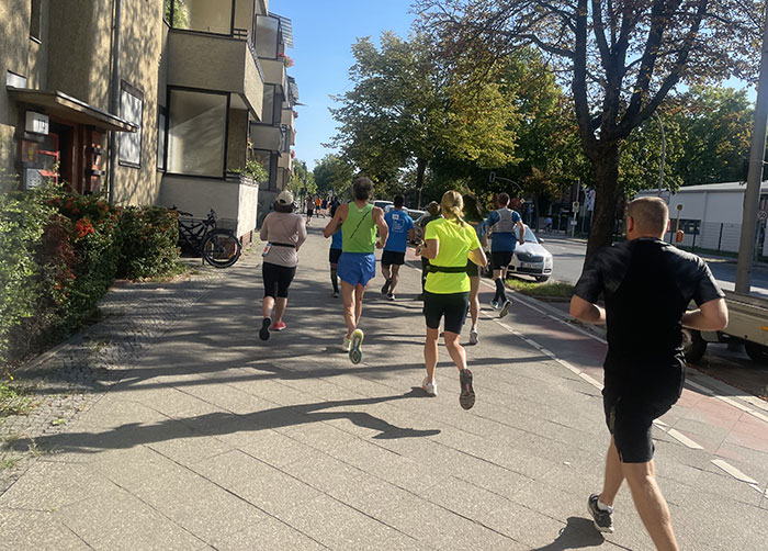 Läuferinnen und Läufer auf einem Fußweg entlang von mehrstöckigen Mietshäusern