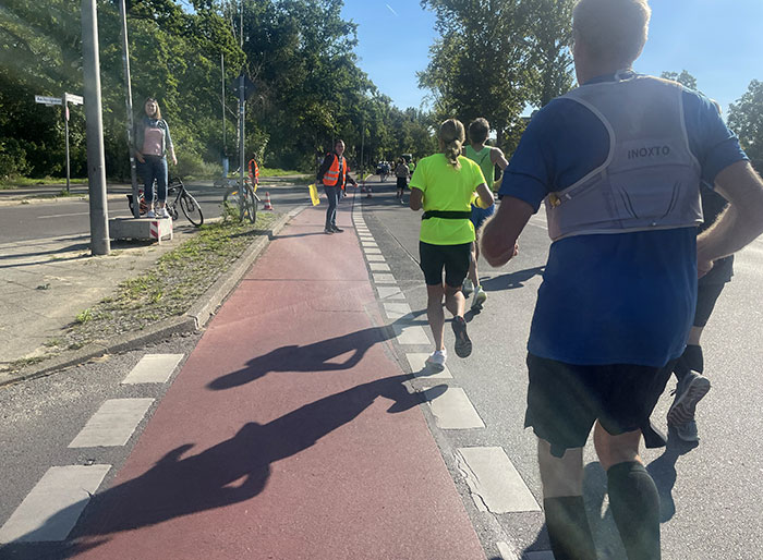 Die Läuferinnen und Läufer werfen lange Schatten auf einen Radweg