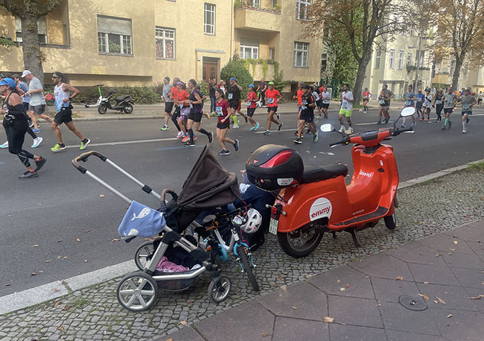 Läuferfeld des Berlin-Marathon, im Vordergrund ein Kinderwagen und ein Miet-Motorroller