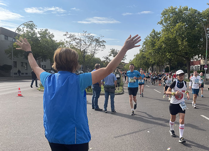 Unterstützerin begrüßt ankommenden Marathon-Läufer mit hoch erhobenen Armen