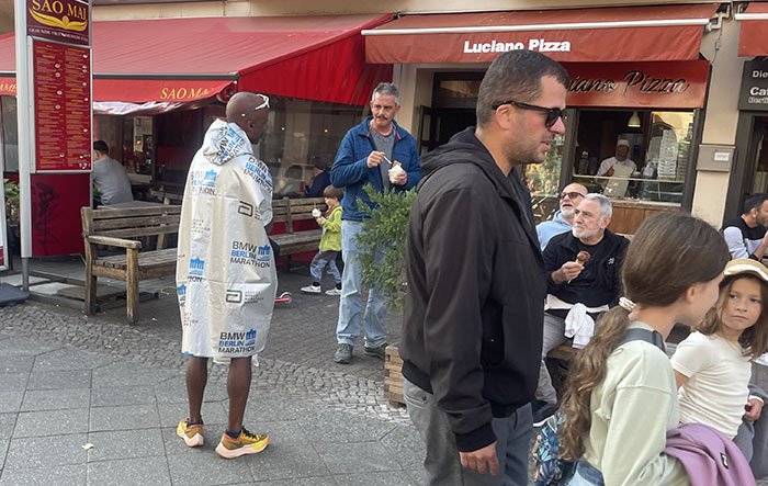 Läufer in einer silbernen Marathon-Decke unterhält sich mit Mann vor einer Pizzeria