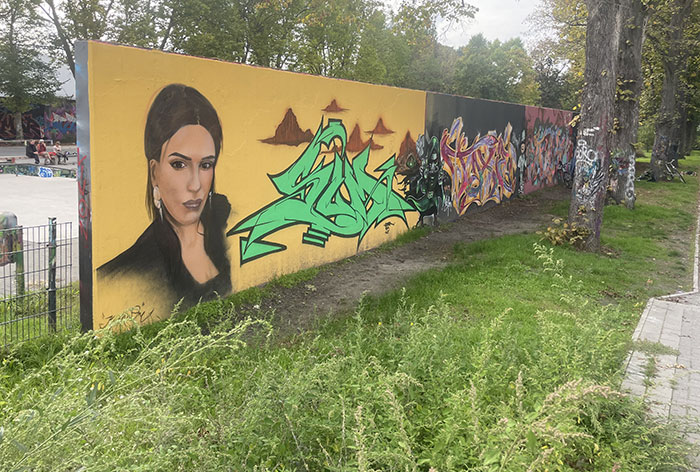 Graffiti-Wand, im Vordergrund ein großes Frauenporträt auf gelbem Grund