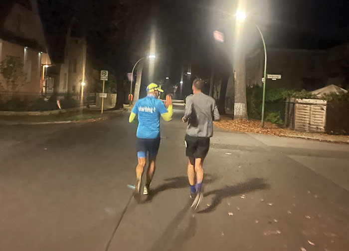 Zwei Läufer auf einer von Laternen beleuchteten Straße in der Morgendunkelheit