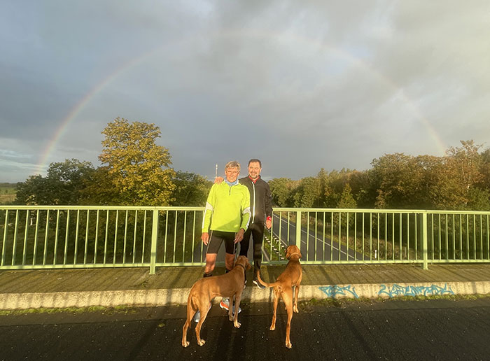 Läufer mit Hunden auf Brücke, dahinter ein Regenbogen