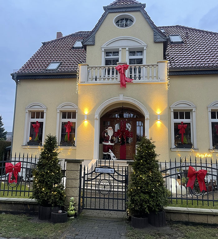 Kleine Villa, die mit großen roten Schleifen weihnachtlich geschmückt ist, im Eingang steht eine Weihnachtsmann-Figur mit Hund