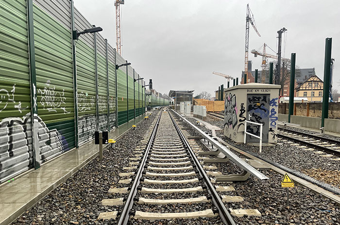 Blick über die neuen Gleise auf den neuen Bahnsteig, an der Seite eine hohe, mit Graffiti beschmierte neue Lärmschutzwand