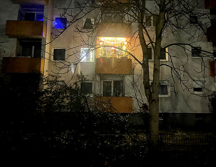 Mehrstöckiges Mietshaus im Dunkeln mit einem hell erleuchteten Balkon mit Weihnachtsdeko