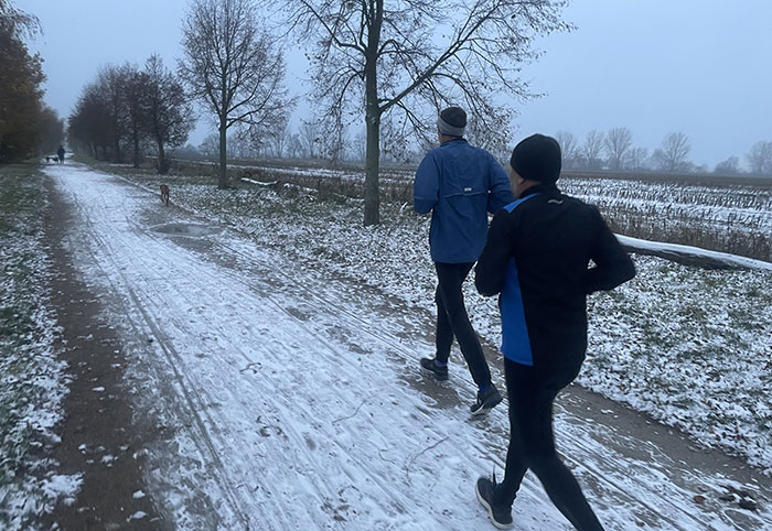 Zwei Läufer auf einem Weg zwischen den Feldern, es liegt eine dünne Schicht Schnee