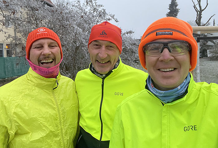 Drei Läufer – alle drei tragen eine neongelbe Laufjacke und eine orange-rote Mütze
