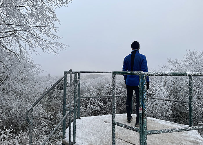 Läufer in blauer Jacke blickt von einem Podest auf der Anhöhe hinunter auf die weiße Landschaft im Nebel