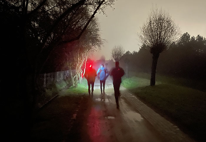 3 Läufer mit Stirnlampen laufen durch einen dunklen Park