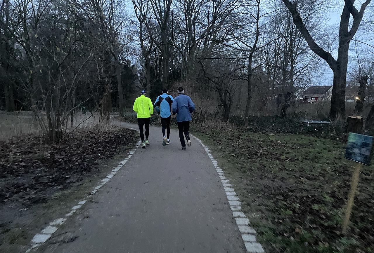 Drei Läufer laufen nebeneinander auf einem Parkweg am frühen Morgen