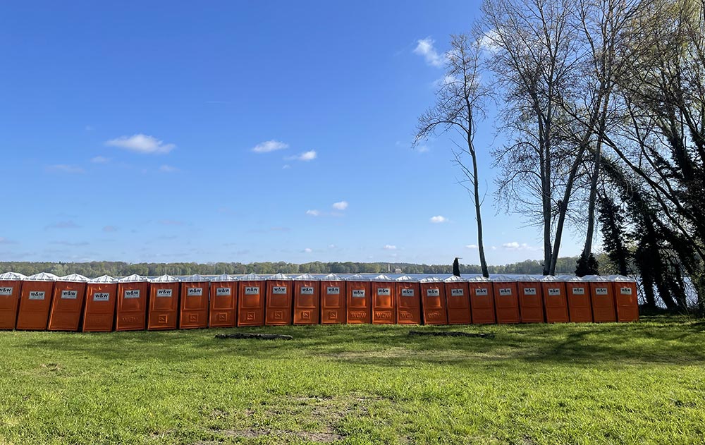 Lange Reihe orangefarbener WC-Häuschen am See vor blauem Himmel