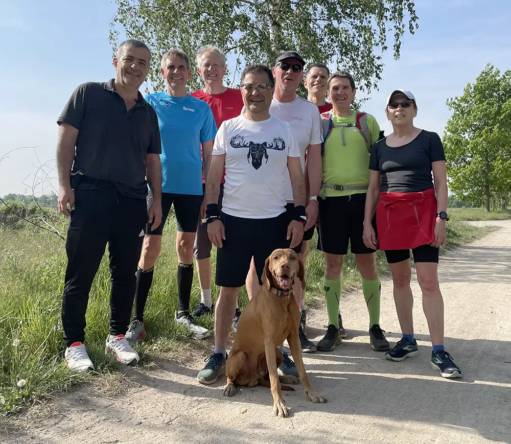 Laufgruppe von 8 Leuten mit Hund posiert auf einem Feldweg