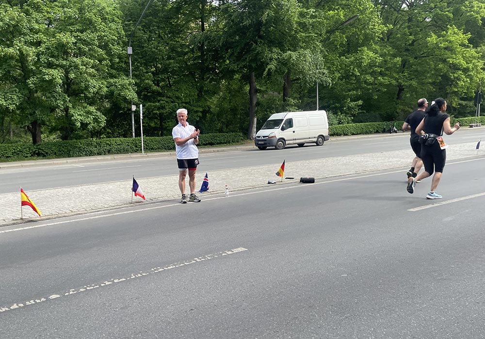 Älterer Mann steht auf dem Mittelstreifen der Straße des 17. Juni, daneben am Boden aufgestellte internationale Flaggen