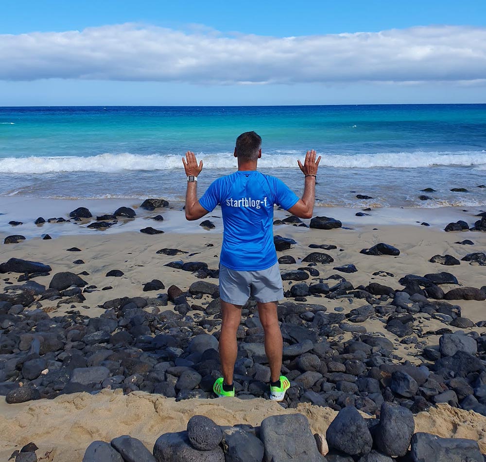 Läufer mit startblog-f-Laufshirt an einem Strand mit Blick auf das grünblaue Meer